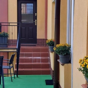 Ukwieciony taras wypoczynkowy przy apartamencie żółtym i zielonym, oraz wejście po czterech schodkach do mieszkania wakacyjnego 